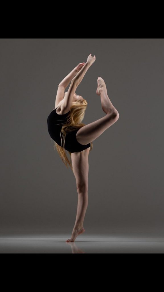 Vivian Hicks in a dance pose, with one leg extended behind her, bent, with her foot over her head.