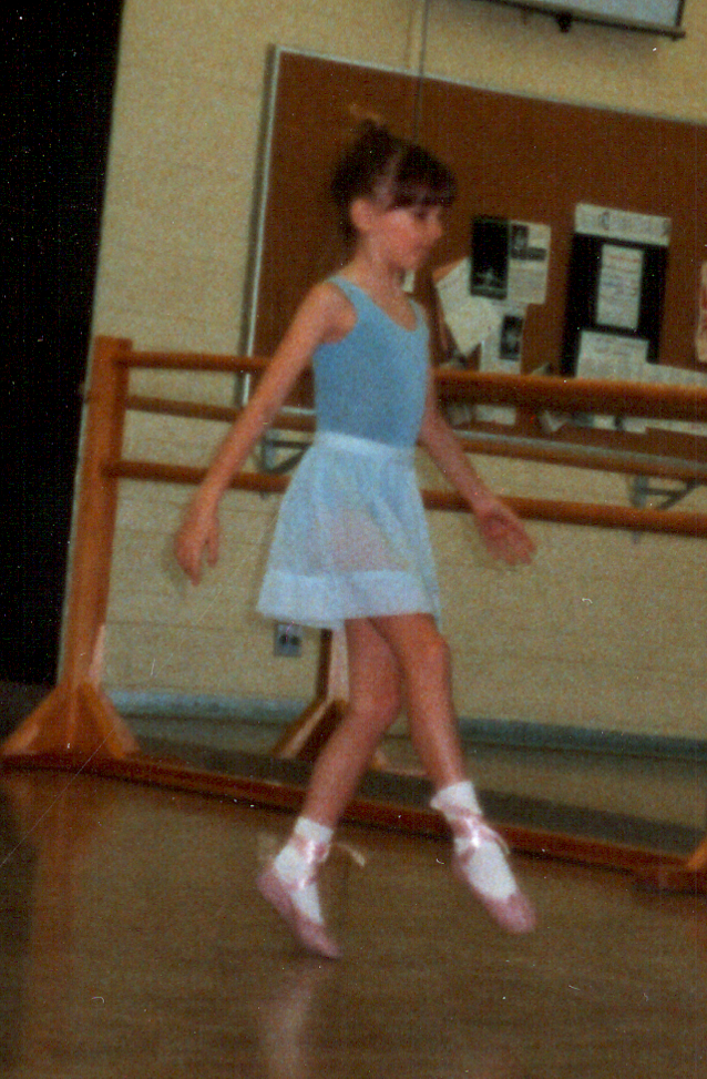 Lori Wolf-Heffner in the single-digit years, wearing a blue bodysuit and ballet skirt, practicing for a ballet exam.