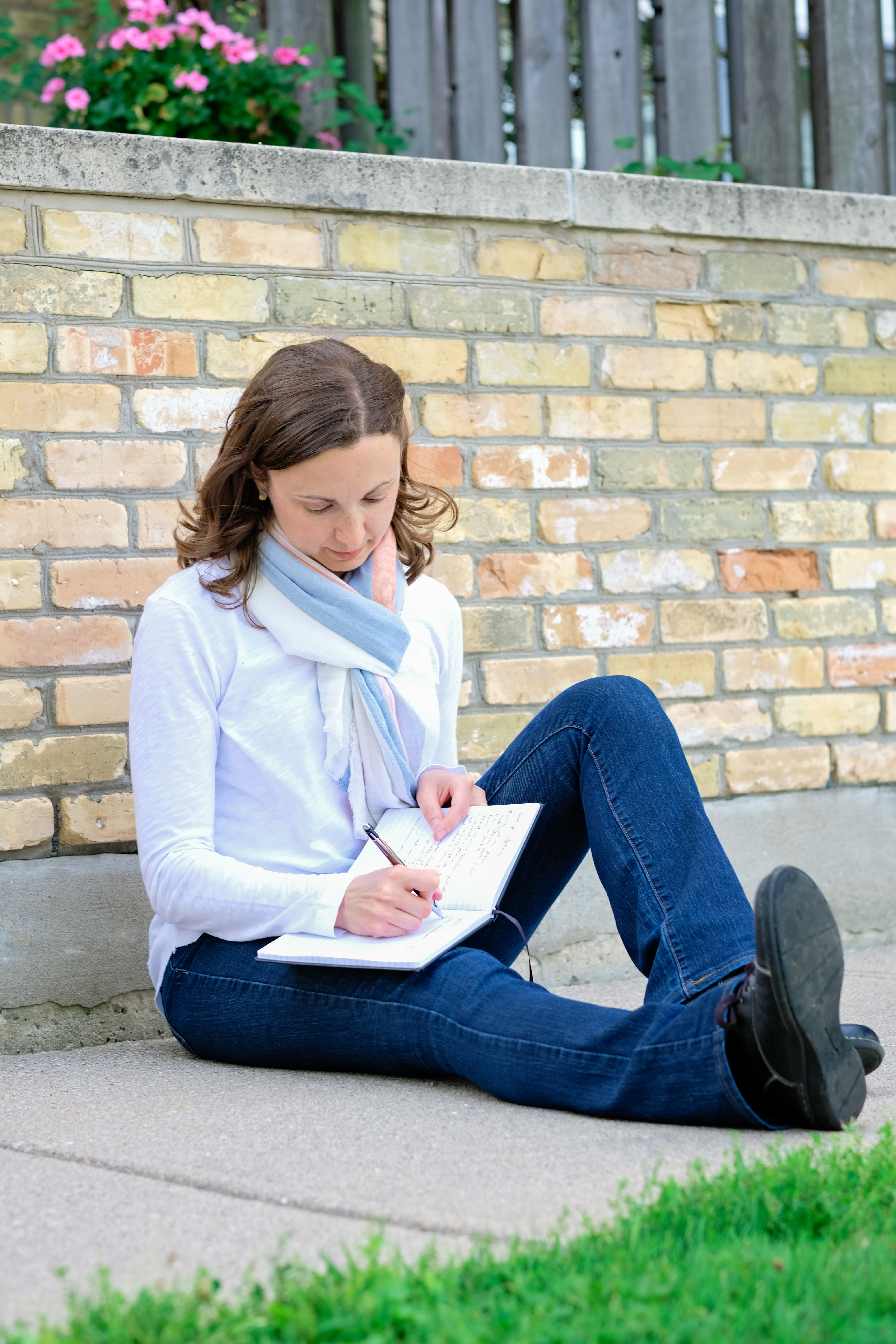Lori Wolf-Heffner sits in front of a brick wall, writing in a journal